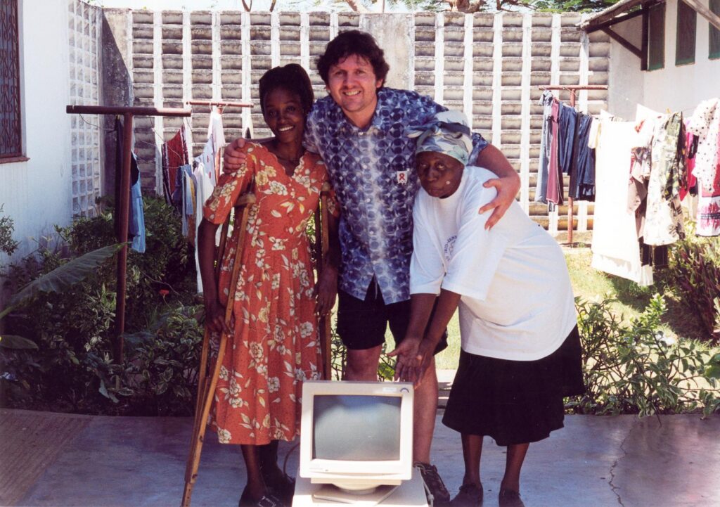 Ross, the founder of Reusing IT, with his arms around 2 ladies with a donated computer.